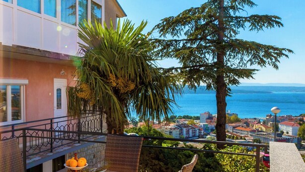 A balcony with a view of the sea, a palm tree, and a building with a balcony. - Modern apartment with beautiful sea views (Crikvenica)