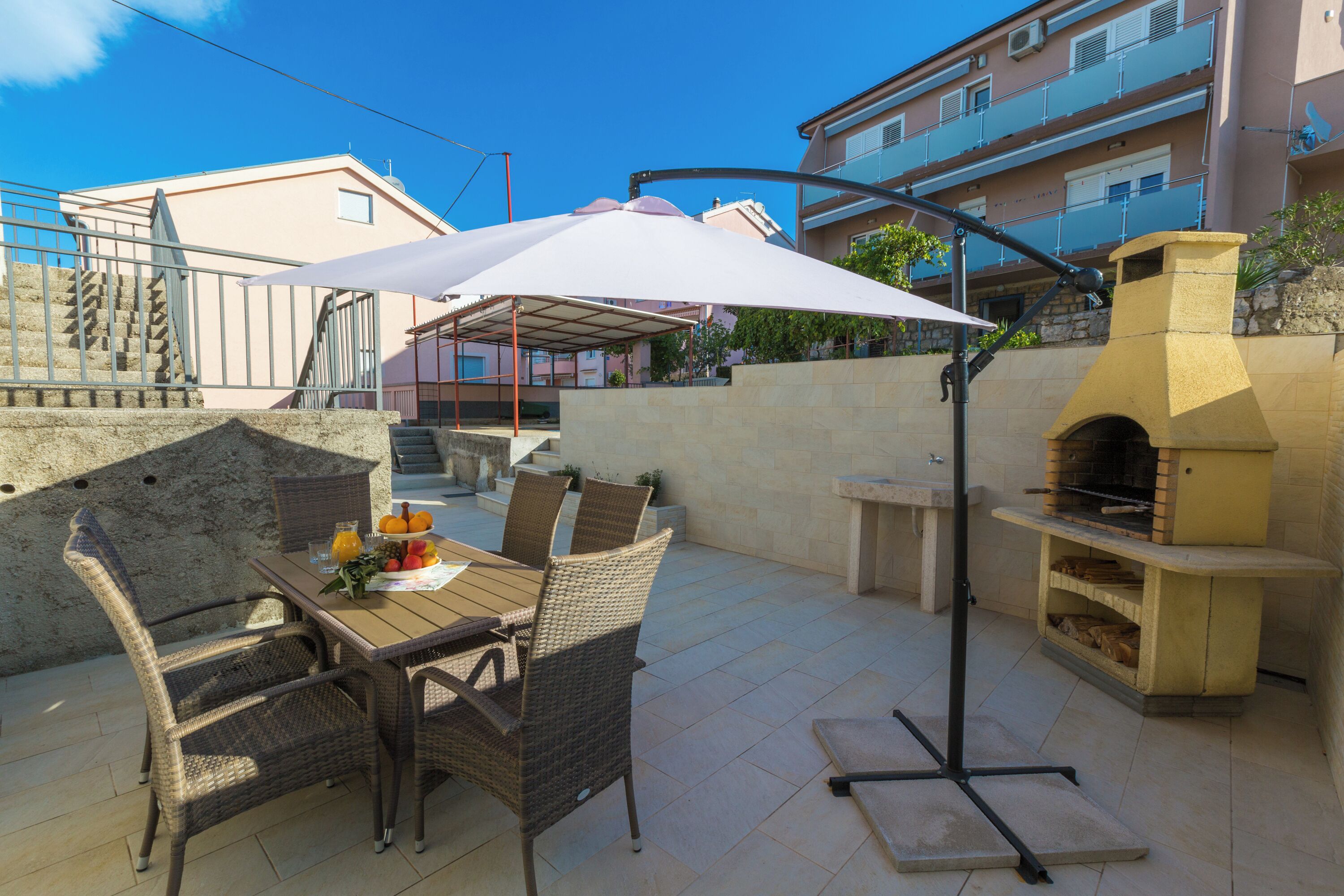 Un patio exterior con mobiliario de mimbre, una mesa con fruta y una parrilla.