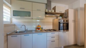 A modern kitchen with a stainless steel sink, a gas stove, and white cabinetry. - Modern apartment with beautiful sea views (Crikvenica)