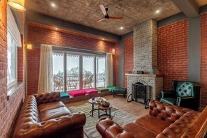 A spacious living area with leather sofas, a fireplace, and a large window with a view. - ELIVAAS Fleur De Lis 4 BHK Villa (Kasauli)