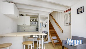 Une cuisine compacte avec un comptoir en bois, des tabourets et un canapé gris agrémenté d’un coussin à rayures.