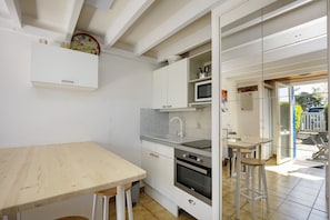 A compact kitchen with a wooden table, white cabinets, a microwave, and a sink. - Charming Maisonnette Ty DaCoLi with Shared Pool, 2-Min Walk to the Beach (Le Pouliguen)
