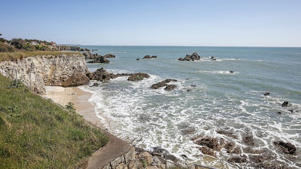 Un paysage côtier caractérisé par des falaises rocheuses, une plage de sable et l’océan.