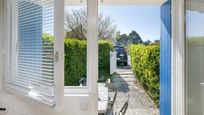 Une vue à travers une porte, avec une table et des chaises à l’intérieur, une porte bleue et un véhicule garé à l’extérieur.
