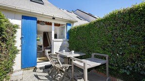 Une terrasse avec une table et des chaises, une porte bleue et une haie.