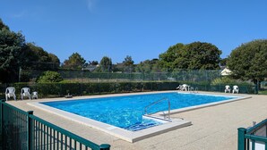 Une piscine rectangulaire avec un escalier en métal, entourée d’une clôture verte et de chaises longues blanches.
