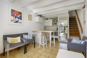 A compact living space with a kitchenette, a dining area, and a staircase leading to an upper level. - Charming Maisonnette Ty DaCoLi with Shared Pool, 2-Min Walk to the Beach (Le Pouliguen)