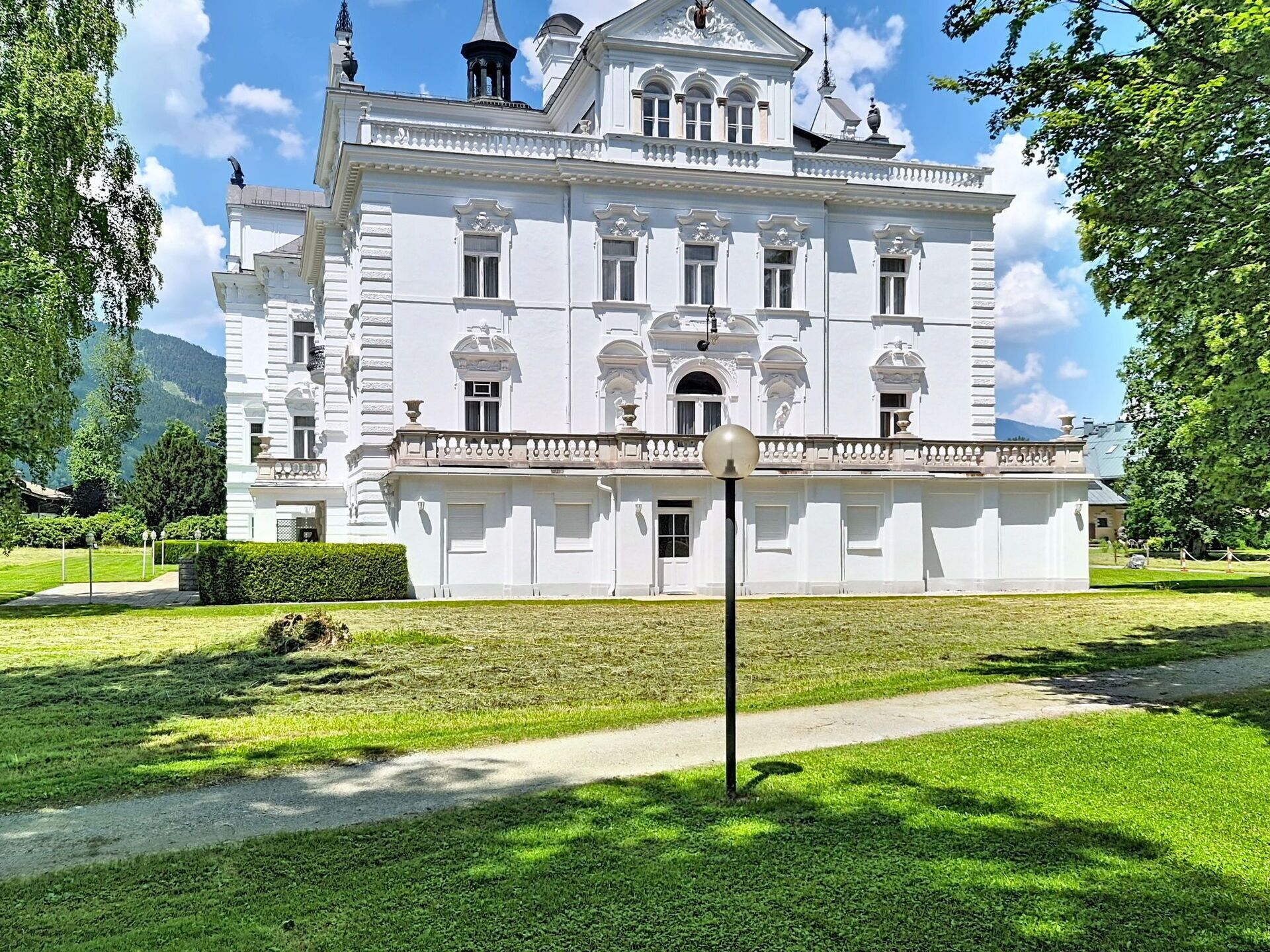 Un grand bâtiment blanc de style classique, doté de nombreuses fenêtres et d’une entrée centrale, et entouré de pelouses et d’arbres bien entretenus.