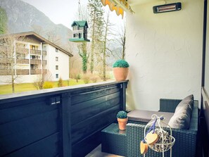 Uma varanda com vista para uma casa, um vaso com planta e um comedouro de pássaros pendurado.
