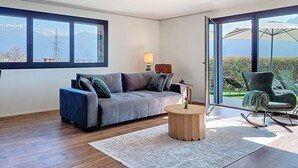 A modern living room with a grey sofa, a wooden coffee table, and a view through large windows. - Lovely apartment for 2 people with WIFI, TV and panoramic view (Riazzino)