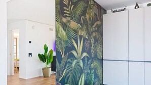 A room with a wooden floor, a large potted plant, and a wall with a tropical leaf pattern. - Lovely apartment for 2 people with WIFI, TV and panoramic view (Riazzino)