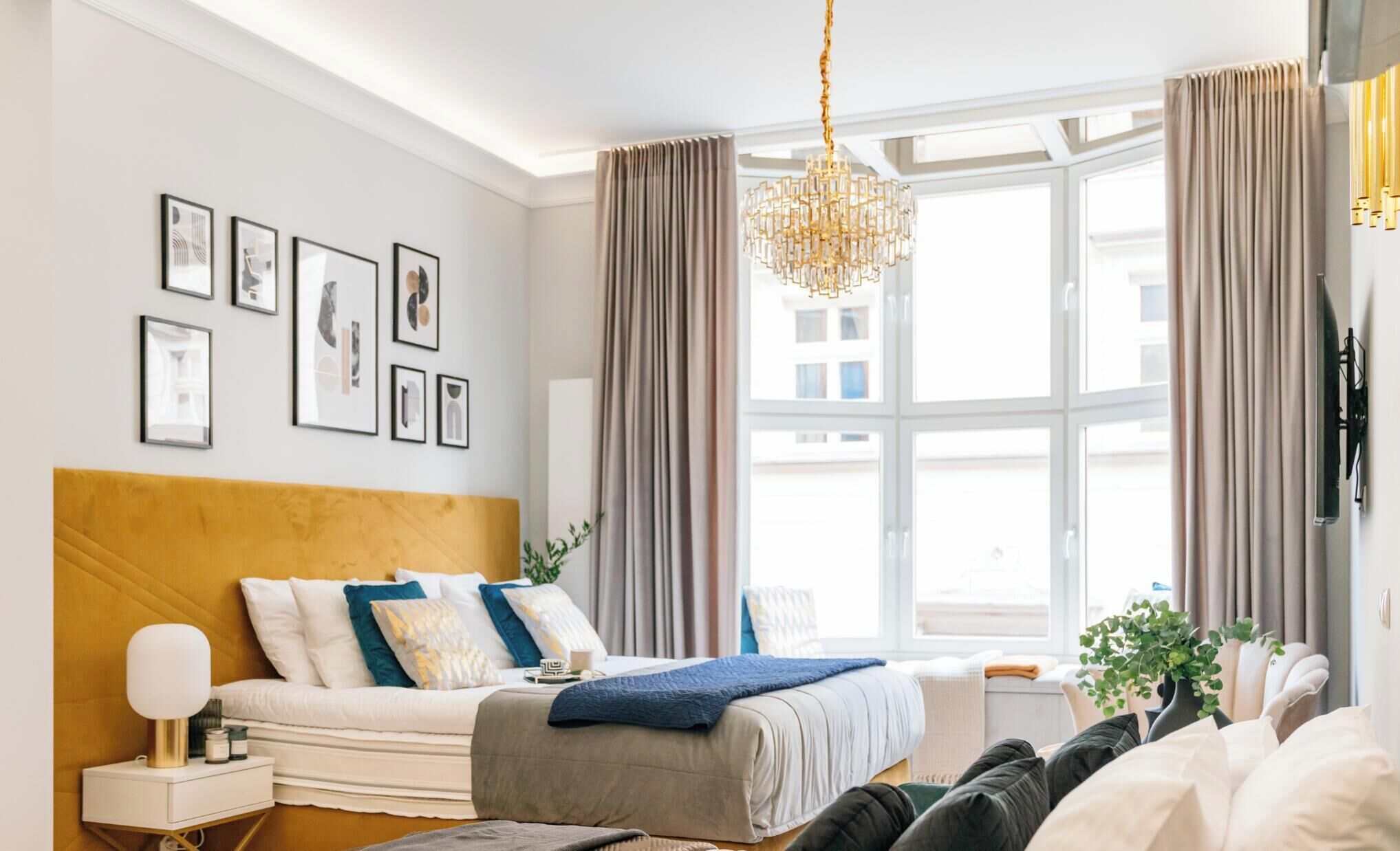 A modern bedroom with a large bed, a bedside table, a nightstand, a chandelier, and a window with curtains.