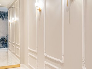 Un pasillo con paredes blancas y detalles dorados, incluyendo apliques de pared y una puerta con pomo dorado.