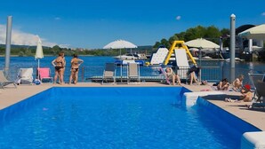 Una piscina con sillas de descanso y sombrillas, un puesto de socorrista y vistas al agua.