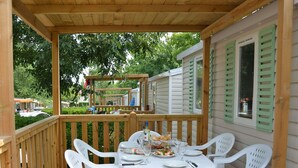 Un área de comedor al aire libre techada con una terraza de madera, sillas de plástico blanco y una mesa lista para una comida.
