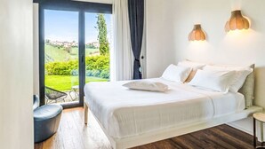 Ein Schlafzimmer mit einem Bett, Blick auf Grünflächen und Gebäude, und einem großen Fenster.