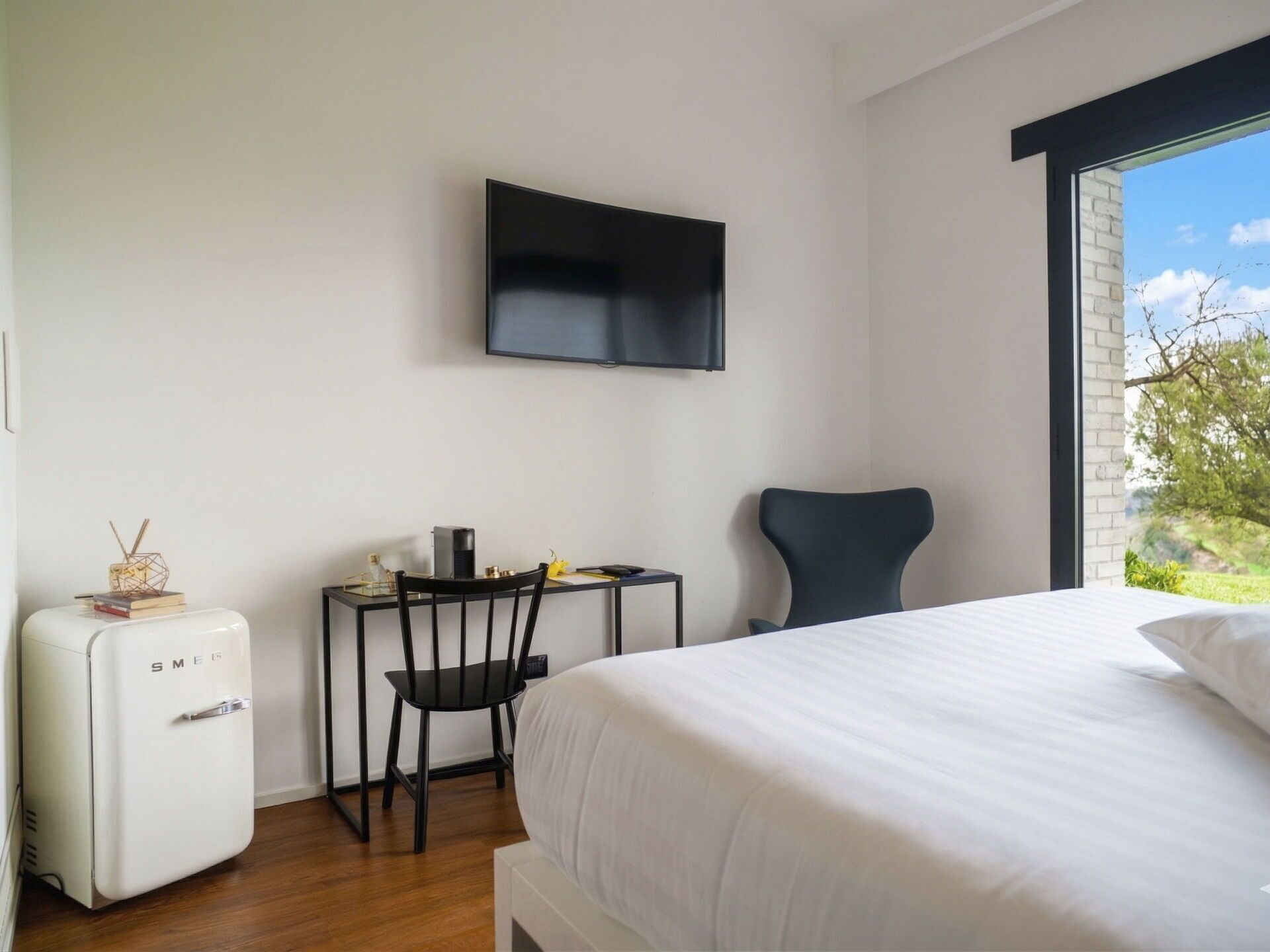 A bedroom with a bed, a desk with a chair, a television on the wall, and a small refrigerator.