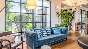 Ein modernes Wohnzimmer mit einem blauen Sofa, großen Fenstern, einer Kristallleuchtre und einem Essbereich.