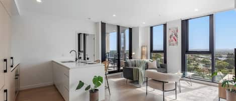 A modern kitchen with a large island, a dining area with a sofa and chairs, and large windows offering a view of the city.
