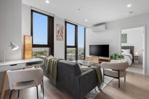 A modern living room with a grey sofa, a flat-screen TV, and a desk with a lamp. - Level 9 Views · 5 min to Austin Hospital | Parking (Ivanhoe)
