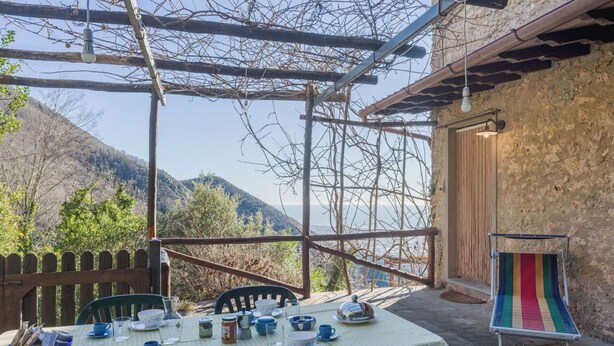 Mesa al aire libre con vista a montañas, una pérgola rústica de madera y una silla colorida a rayas.