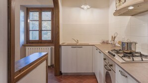 Una cocina con ventana, gabinetes blancos, estufa y lámpara colgante.