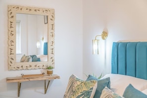 Un dormitorio con cama, espejo, mesita de noche y lámpara de pared.