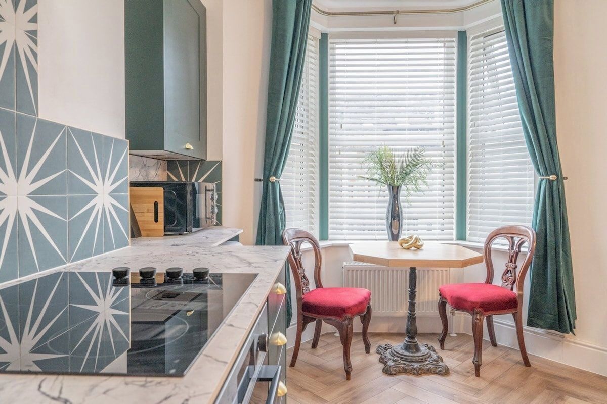 A kitchen with a stove, a dining table with chairs, and a window with curtains.
