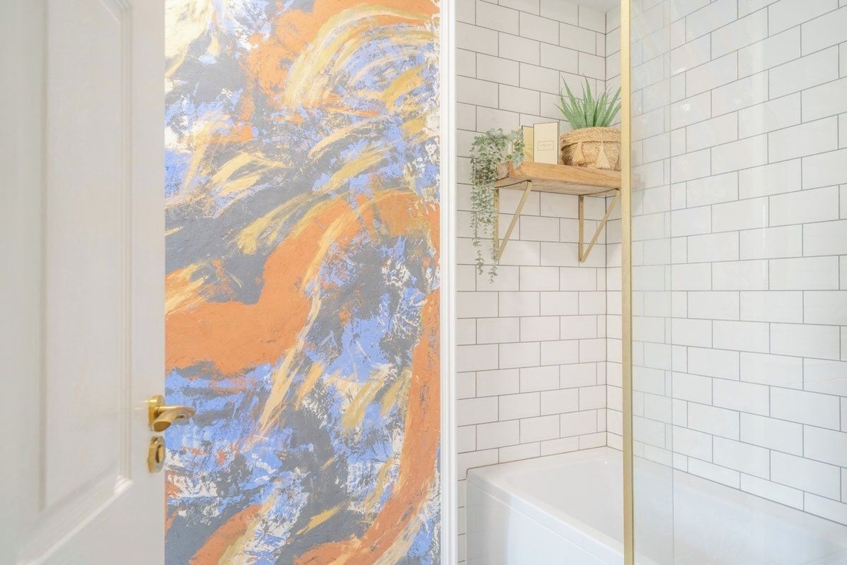A bathroom with white tiled walls, a white bathtub, and a shelf with plants and books.