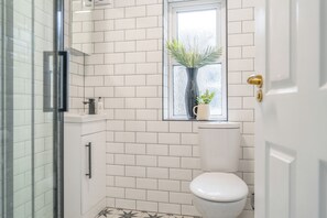 A bathroom with white subway tiles, a toilet, a window with a plant, and a shower area. - Gorgeous 3 Bed House Lancashire (Morecambe)