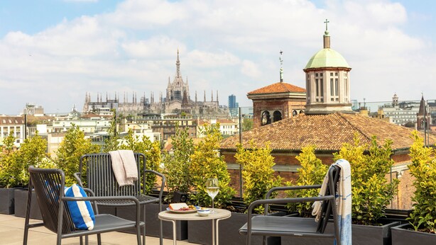 A rooftop terrace with two chairs, a table, and a glass of wine. In the background, there is a cityscape with a prominent church and a tall building. - Bob W Milan Crocetta (Milan)