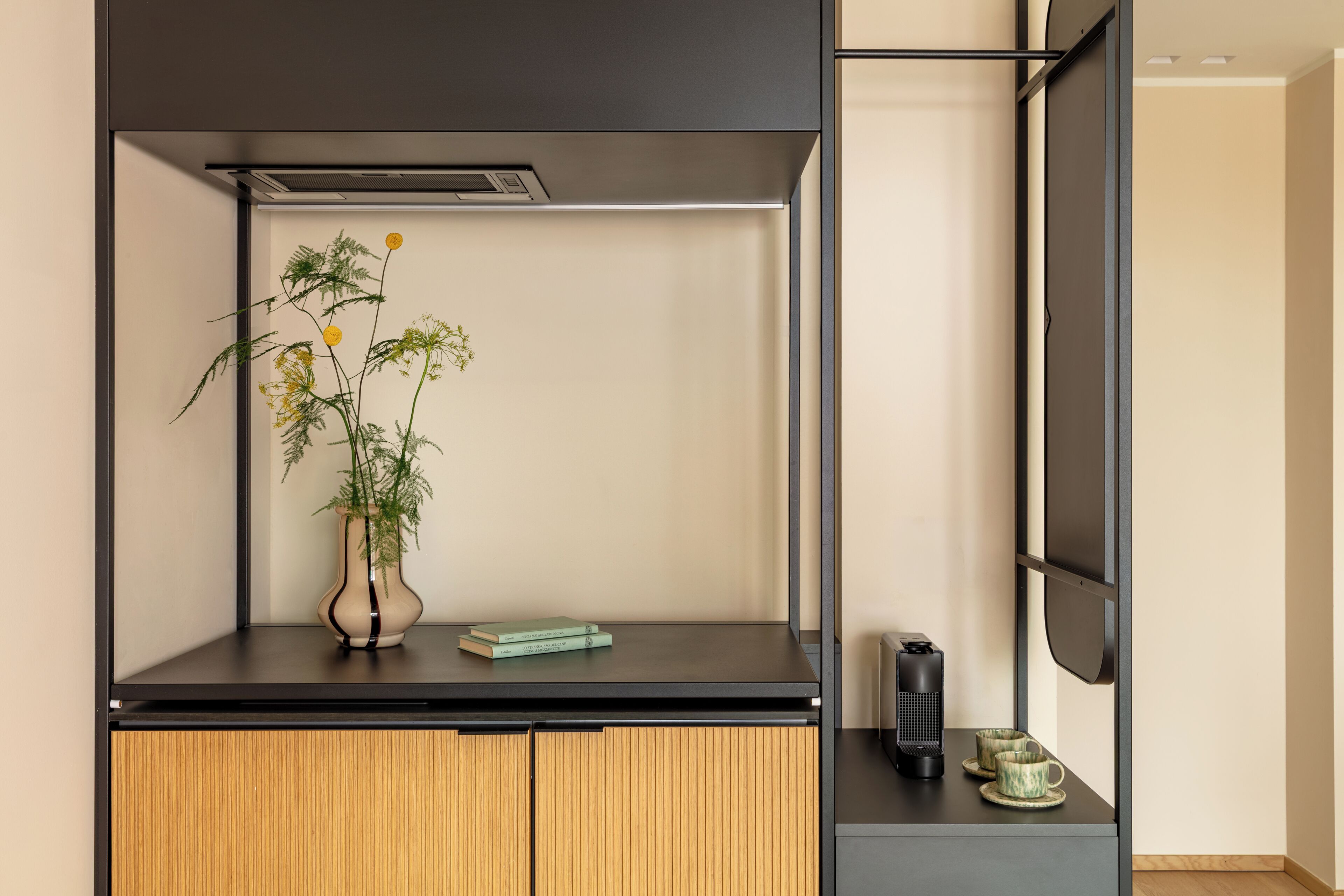 Une chambre moderne avec un bureau noir, une armoire en bois, une plante en pot, un livre, un haut-parleur et une tasse.