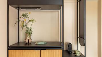 Une chambre moderne avec un bureau noir, une armoire en bois, une plante en pot, un livre, un haut-parleur et une tasse.