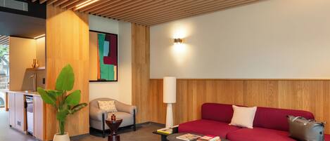 Una habitación moderna con techo de madera, un sofá rojo, un sillón gris, una mesa de centro, una lámpara y una planta.