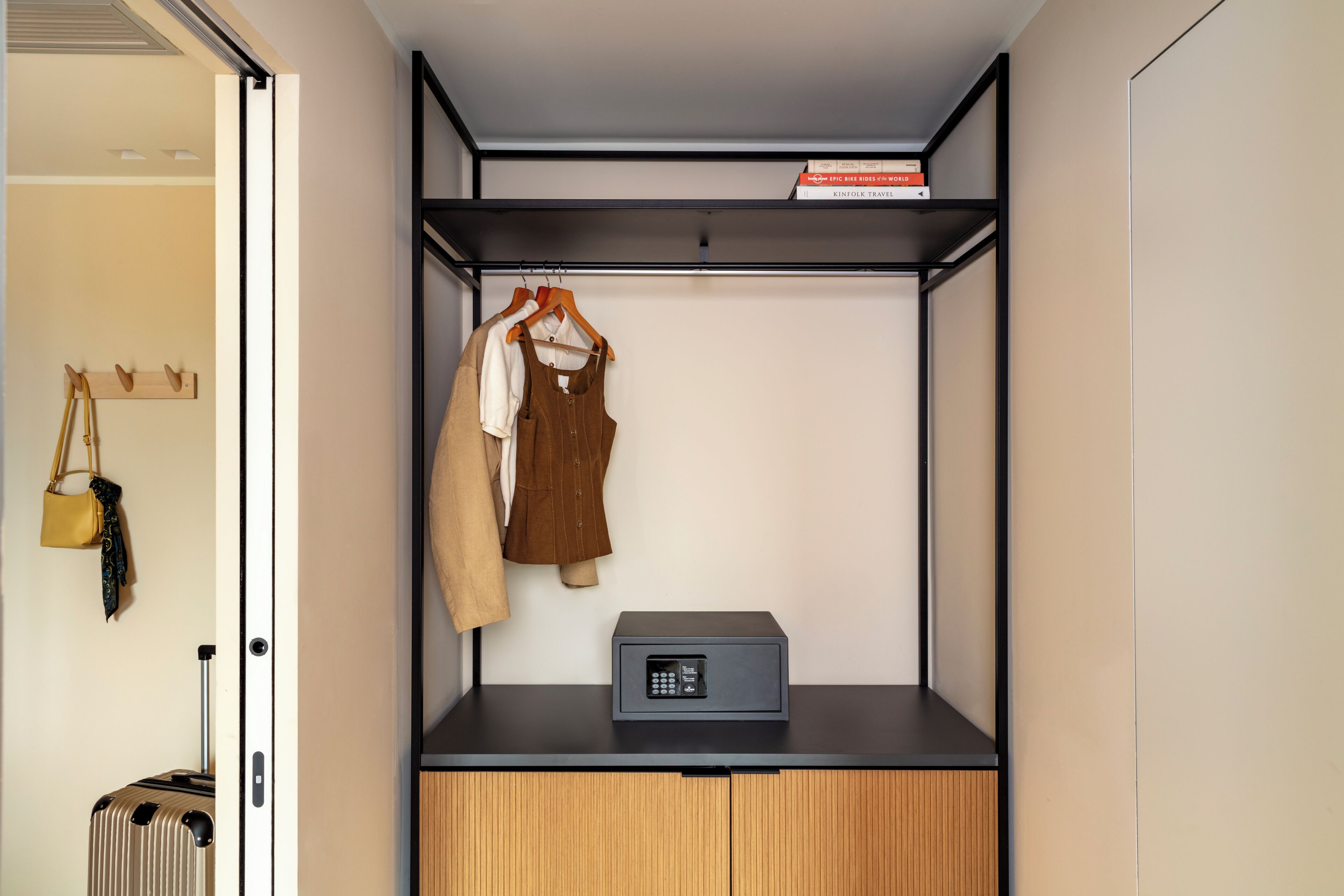 A compact room with a wardrobe, a suitcase, a coat rack, and a small table with a device.
