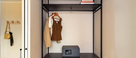 A compact room with a wardrobe, a suitcase, a coat rack, and a small table with a device.