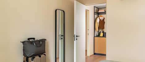 Una habitación de hotel con cama, maleta, espejo y una puerta abierta hacia el baño.