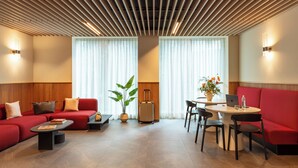 A modern hotel lobby with a red sofa, a table with chairs, a potted plant, and a suitcase. - Bob W Milan Crocetta (Milan)