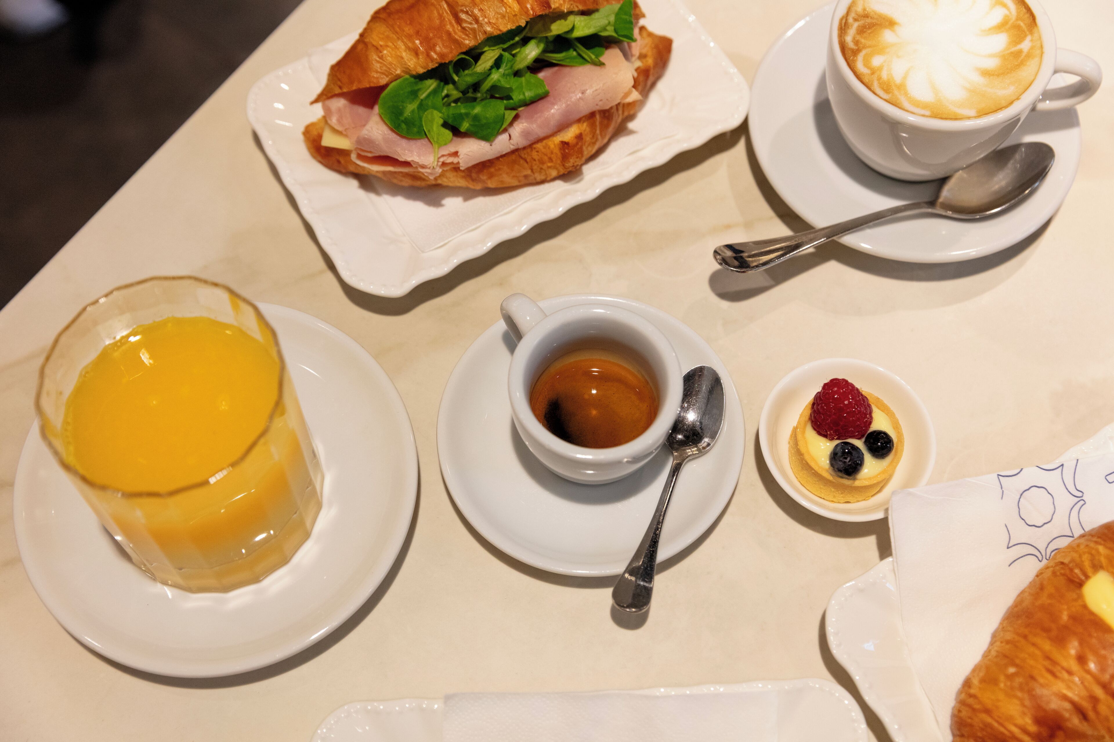 A table with a sandwich, a cup of coffee, a dessert, and a plate with a beverage.