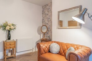 A room with a leather sofa, a mirror, a lamp, a vase with flowers, and a radiator.