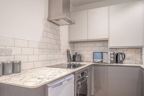 A modern kitchen with white tiles, a marble countertop, a built-in oven, a microwave, and a coffee machine. - Fabulous New 1 Bedroom Ground Floor Flat (Morecambe)