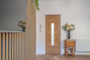 A room with a wooden door, a small wooden table with a vase of flowers, and a radiator on the wall. - Fabulous New 1 Bedroom Ground Floor Flat (Morecambe)