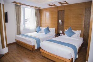 A hotel room with two beds, wooden flooring, a large window with curtains, and a flat-screen TV mounted on the wall. - New Hotel Tradition (Kathmandu)