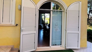 A building entrance with a glass door and two white shutters, a tiled floor, and a green mat.