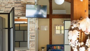 A room with a stone wall, a bed with a blue bedspread, a television mounted on the wall, and a ceiling fan.