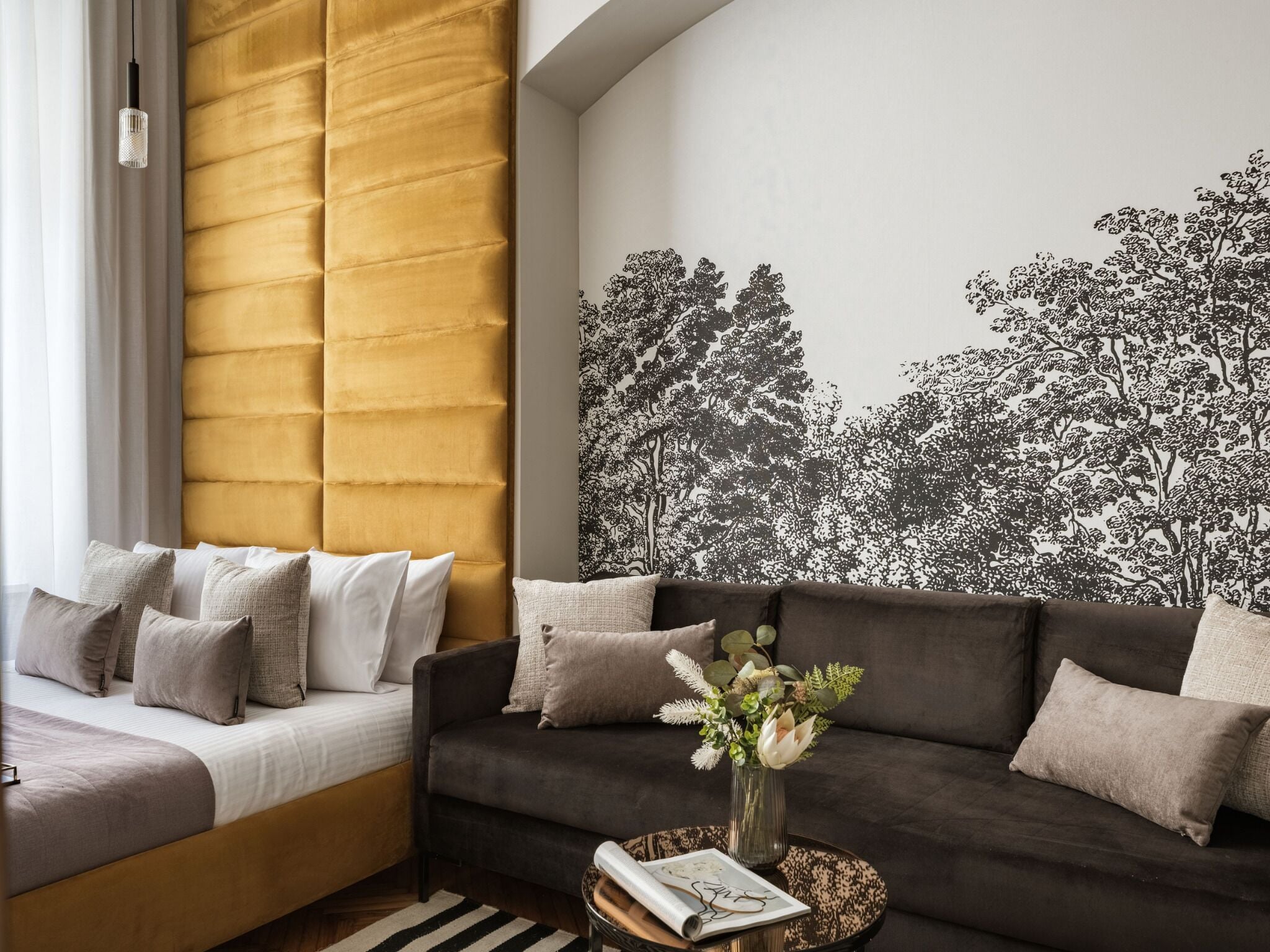 A modern living room with a sofa, a bed, and a wall with a tree pattern.