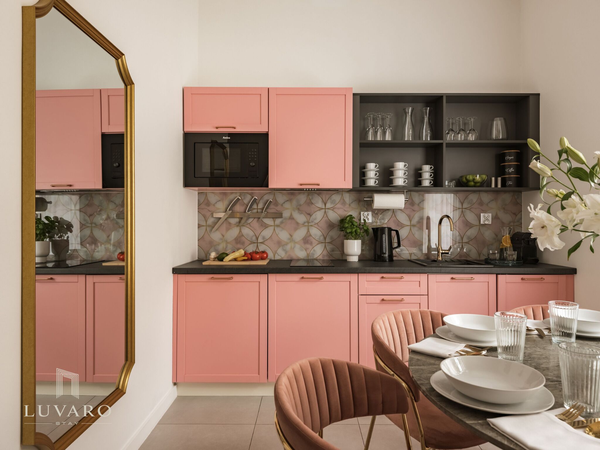 A modern kitchen with pink cabinets, a black microwave, and a dining area with a table set for two.