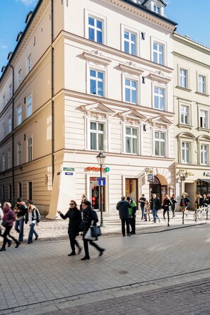 Un edificio storico dall'architettura classica, con una strada acciottolata e persone che vi passeggiano.