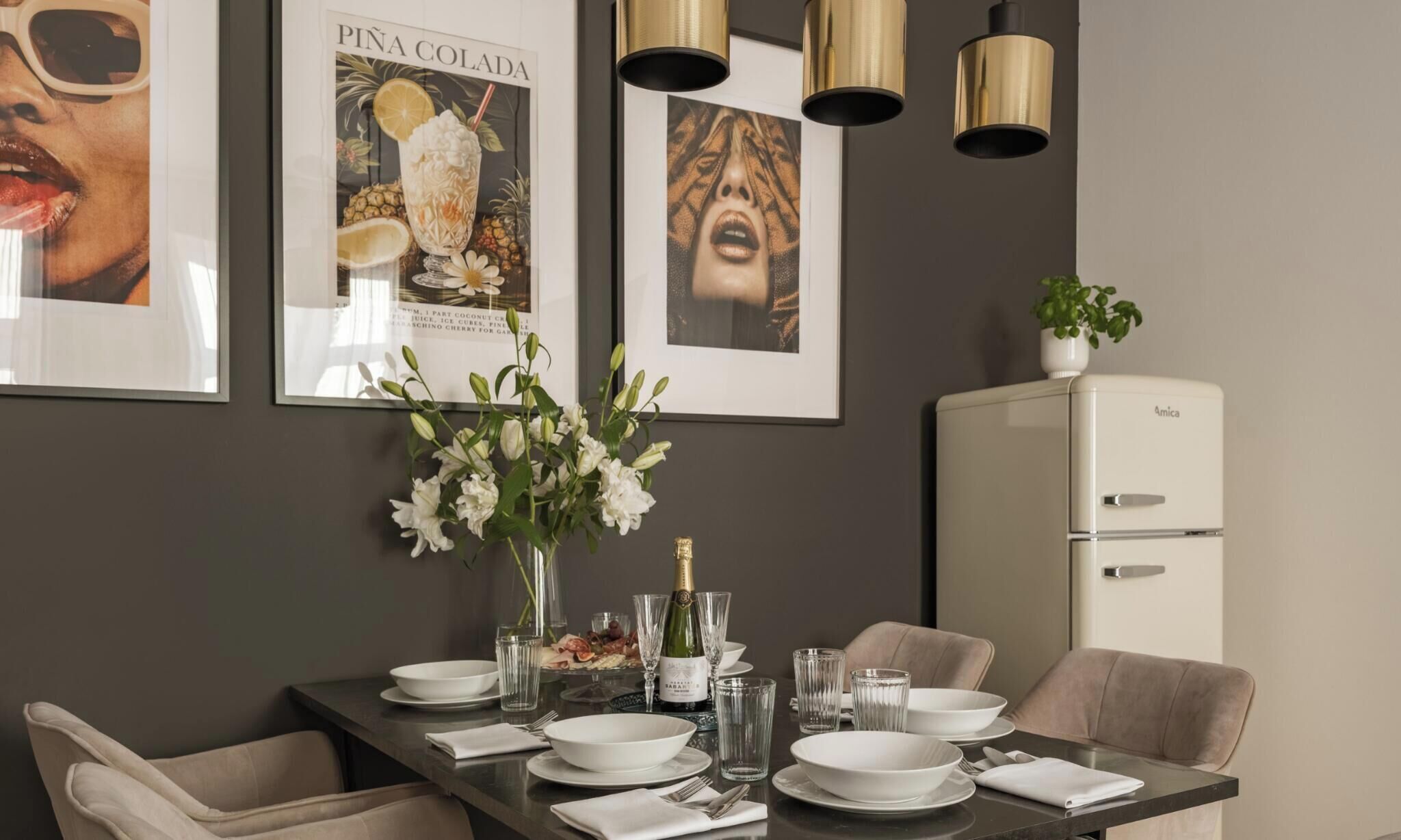 Un comedor con una mesa lista para cuatro personas, un cuadro en la pared y un refrigerador al fondo.