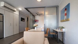 Moderni hotellihuone, jossa on sohva, ruokapöytä, televisio ja maalaus majakasta.